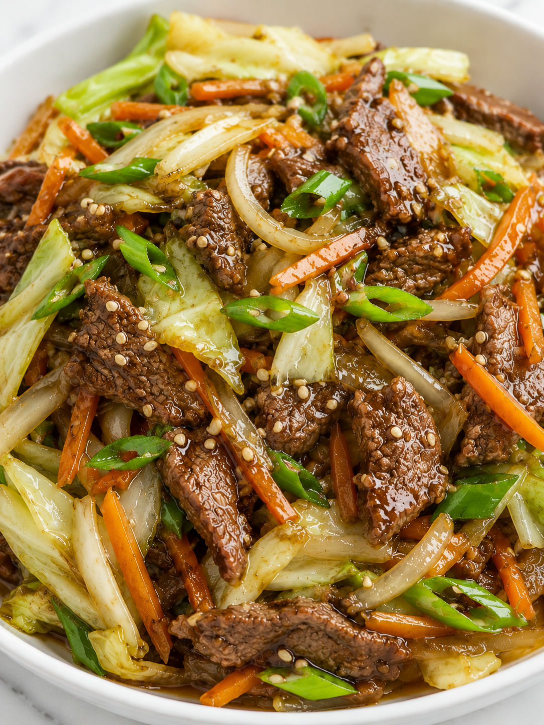Saucy beef cabbage stir-fry with carrots and sesame seeds in a white bowl