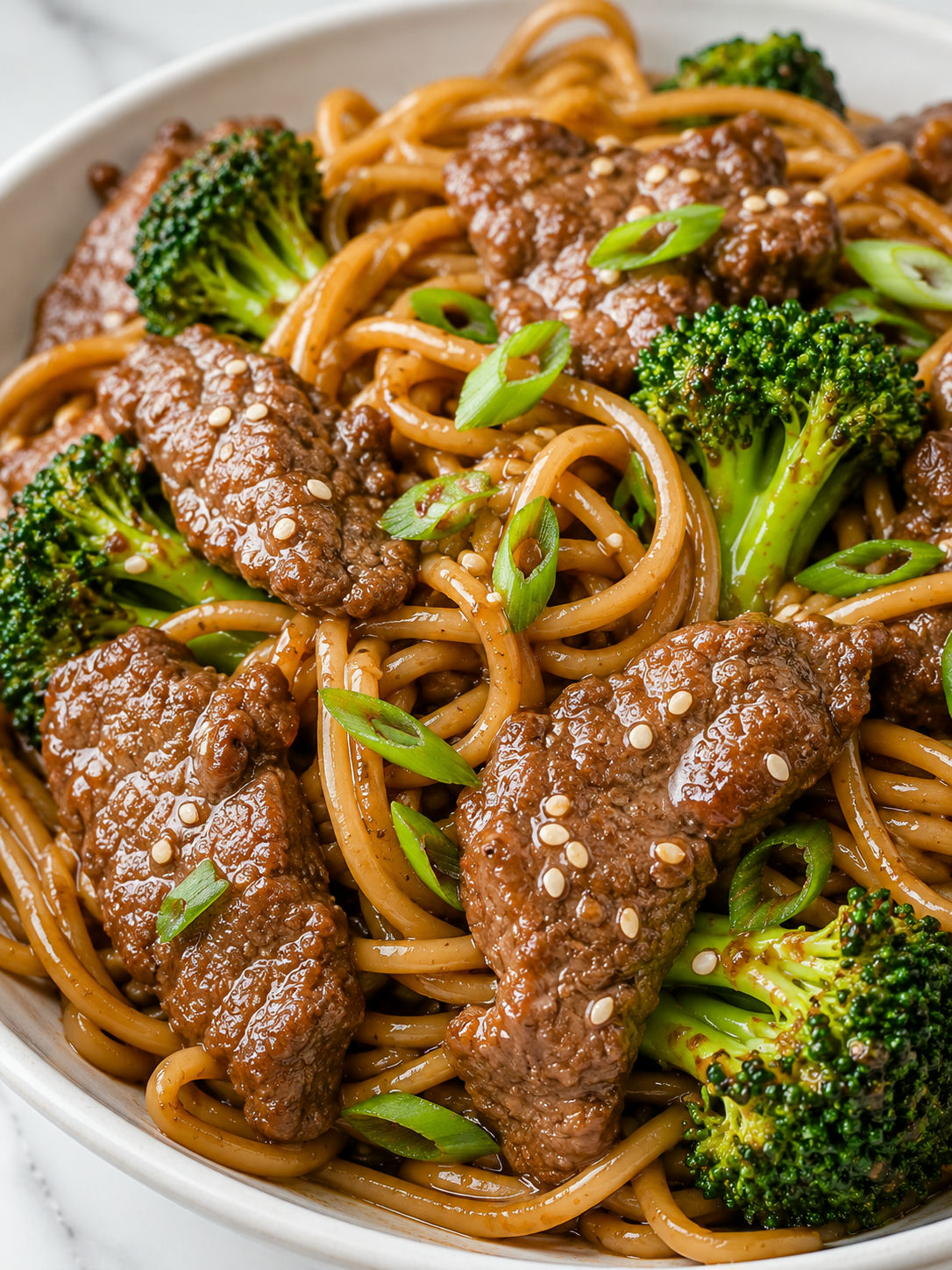 Glossy beef broccoli noodles with chopsticks, scallions, and sesame seeds