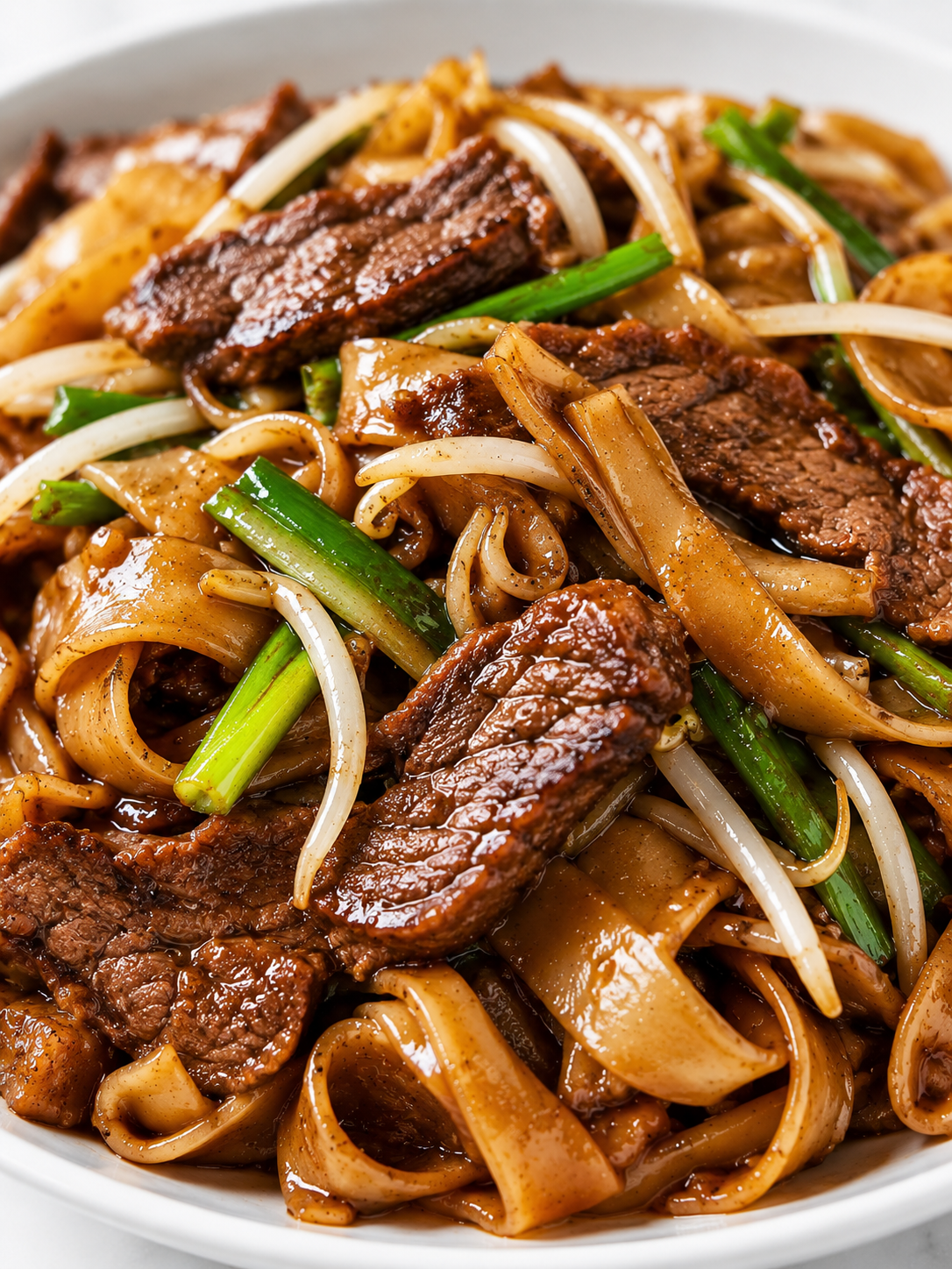 Glossy beef chow fun noodles with browned beef, sprouts, and scallions
