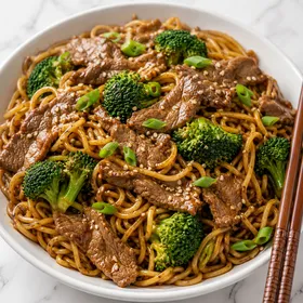 Beef broccoli noodles with green onions and sesame seeds in a white bowl