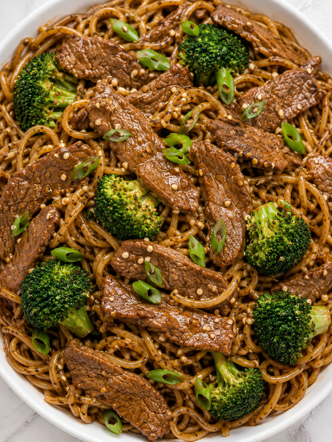 Top-down beef broccoli noodles with glossy sauce, sesame seeds, and green onions