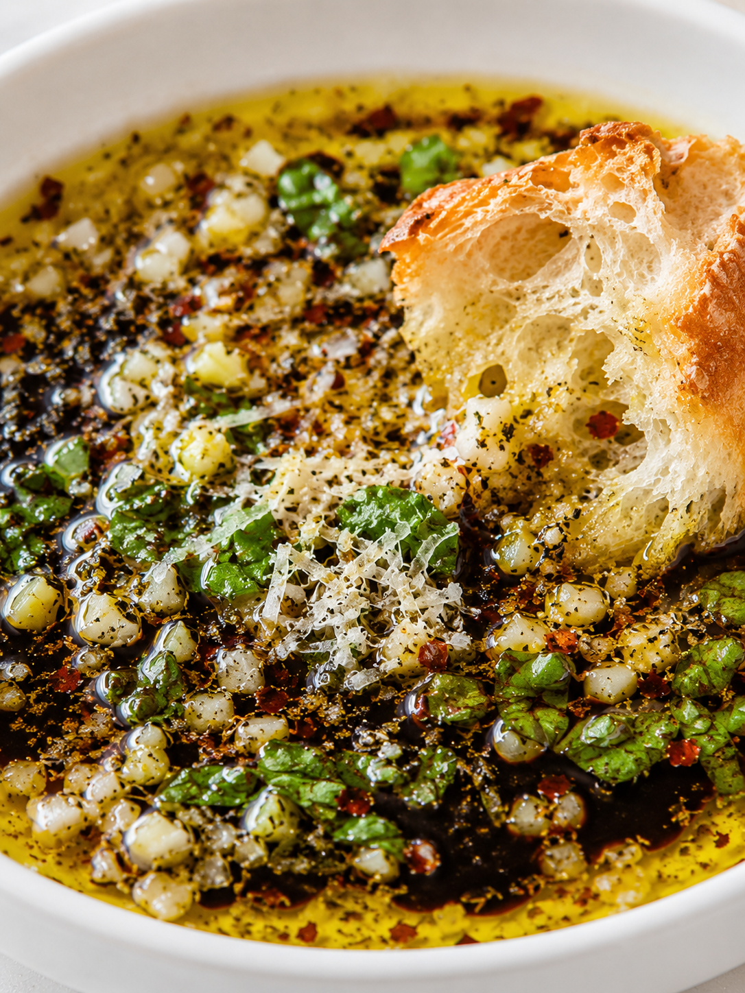 Bread dipping into garlicky herb olive oil with Parmesan