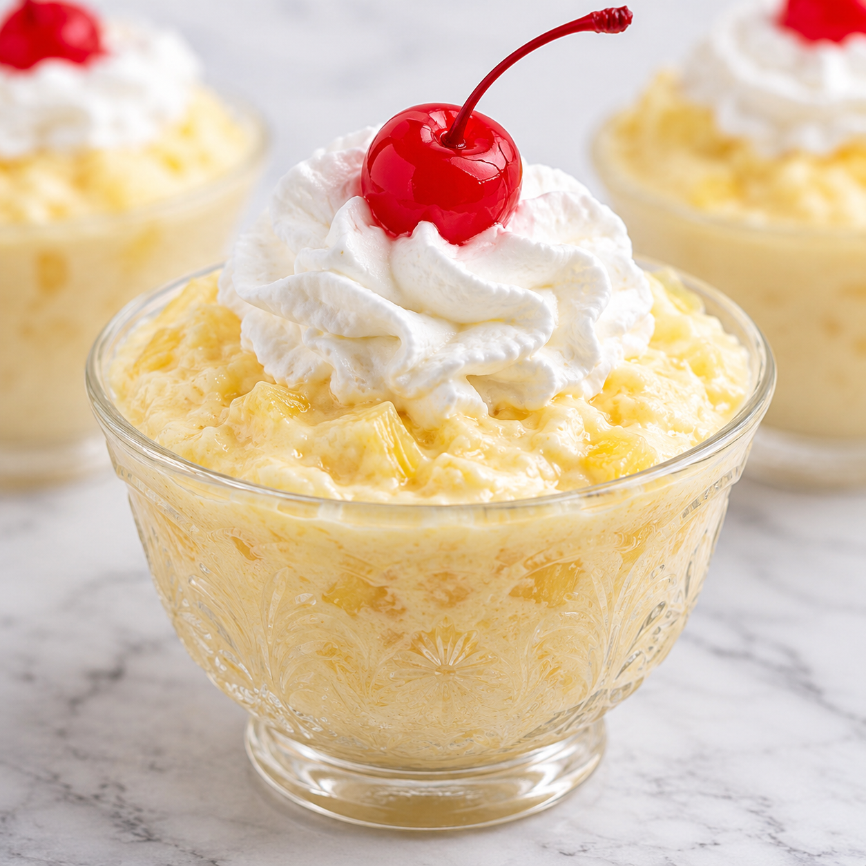 Creamy pineapple dessert with whipped topping and a cherry in a glass cup