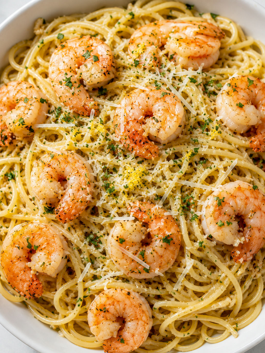 Garlic shrimp pasta filling a bowl with parsley, Parmesan, and lemon zest
