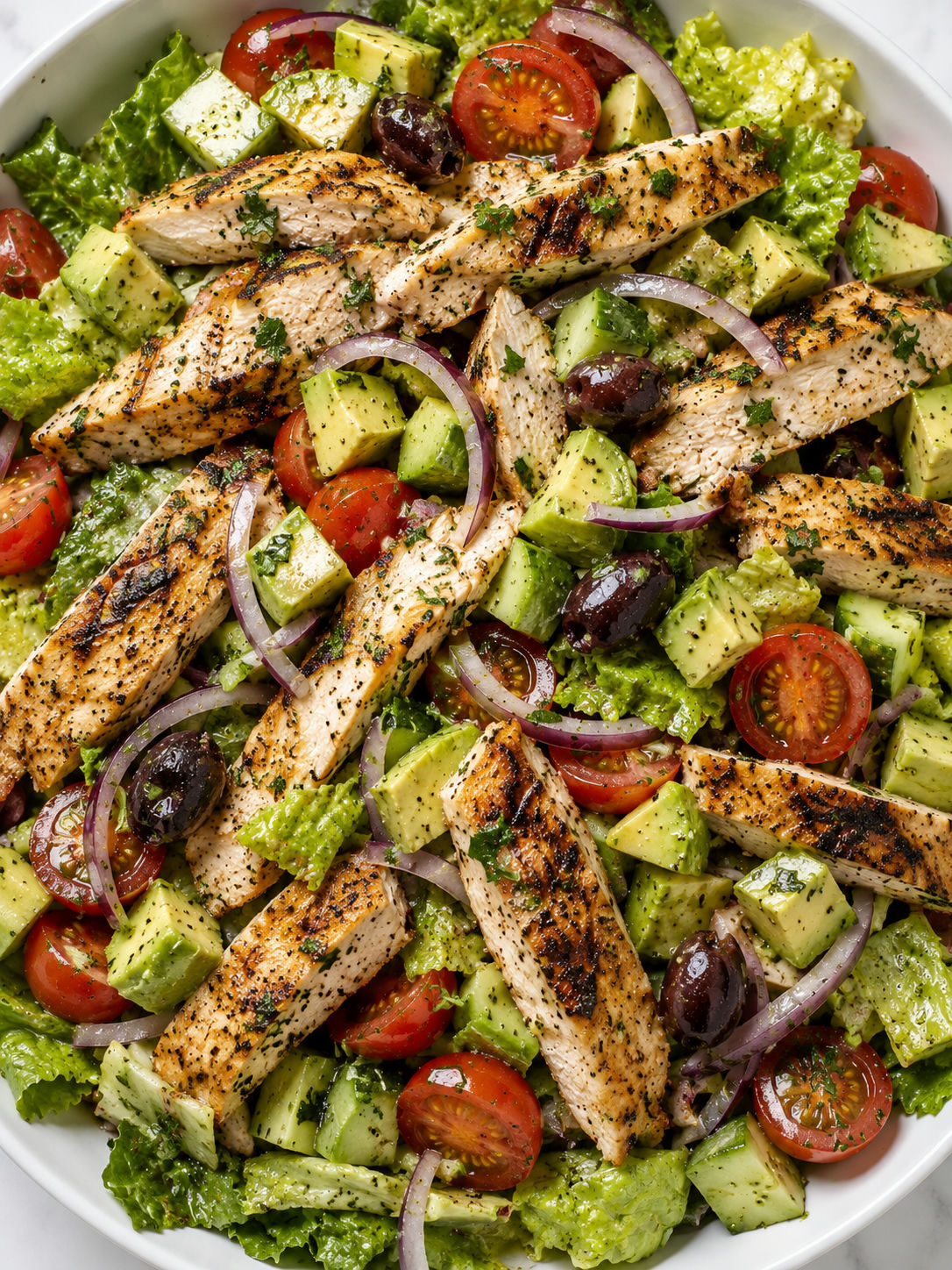 Top-down grilled chicken salad with avocado, tomatoes, olives, and herbs