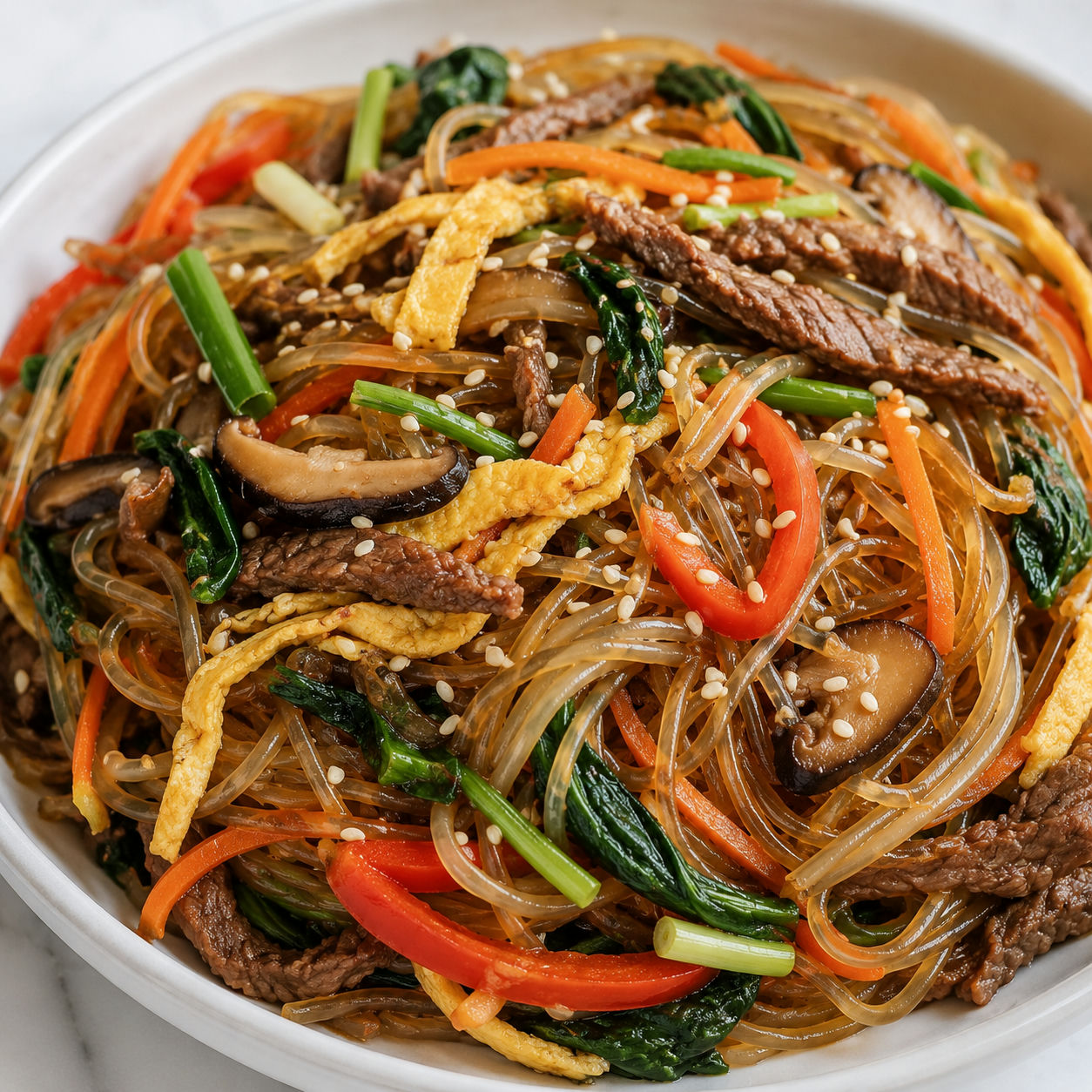 Japchae with beef, spinach, carrots, egg ribbons, and sesame seeds