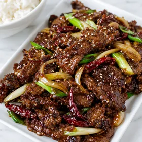 Glossy Mongolian Beef with scallions and sesame on a white plate