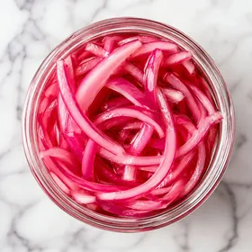Bright pickled red onions in a glass jar with glossy pink brine