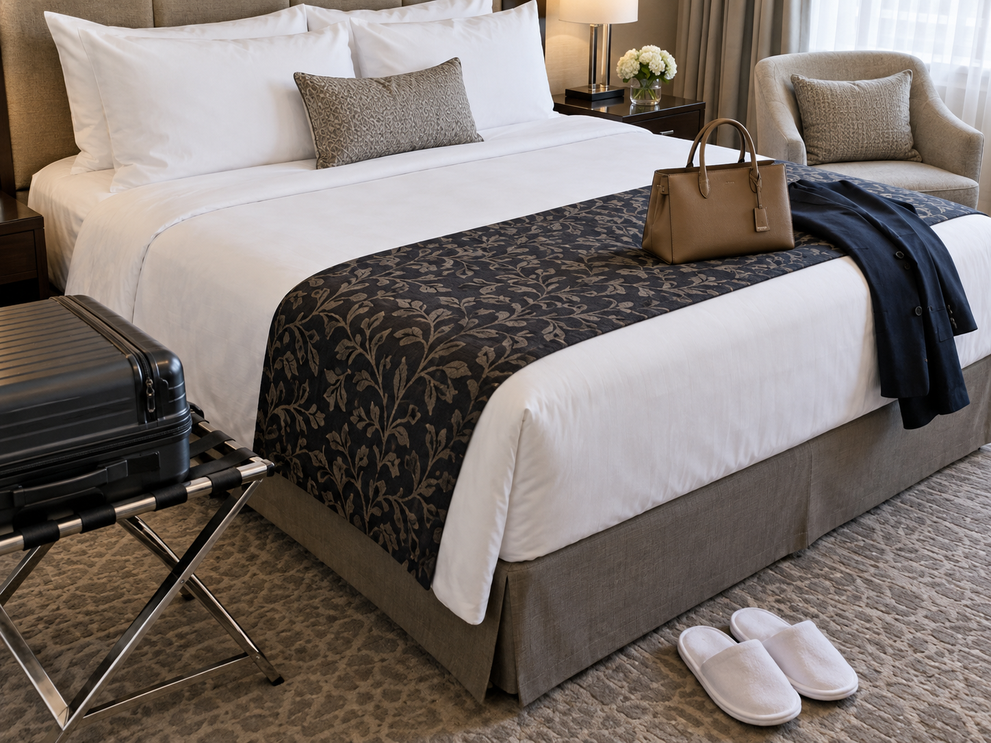 Hotel bed runner with suitcase, slippers, handbag, and chair nearby
