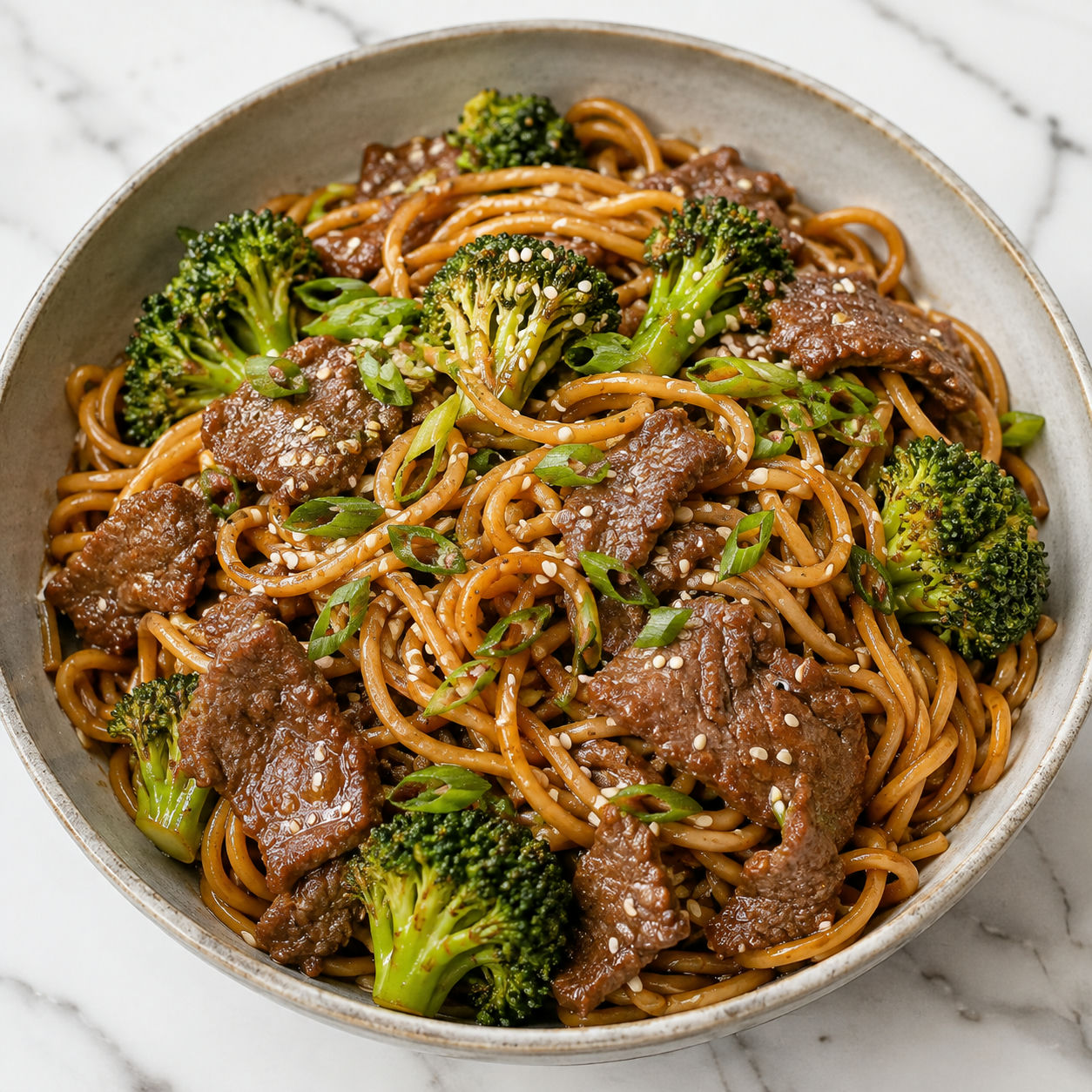 Beef broccoli noodles with scallions and sesame seeds in a shallow bowl