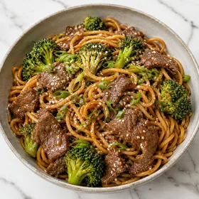 Beef broccoli noodles with scallions and sesame seeds in a shallow bowl