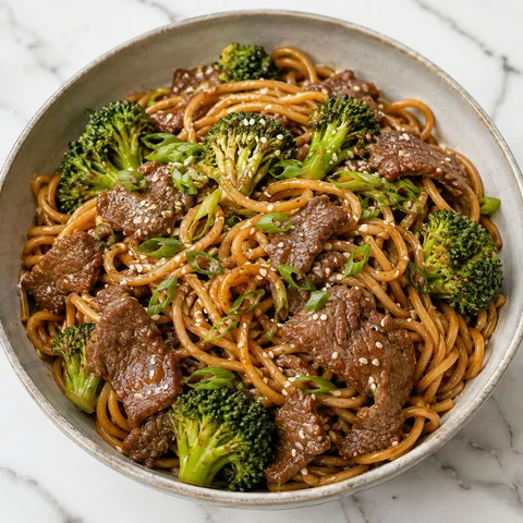 Beef broccoli noodles with scallions and sesame seeds in a shallow bowl