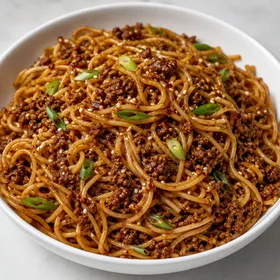 Spicy garlic beef noodles with scallions and sesame in a white bowl