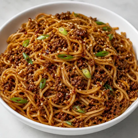 Spicy garlic beef noodles with scallions and sesame in a white bowl